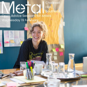 There is a smiling young woman seated at a table. The table is cluttered with writing materials and glassware. Behind, there is a teal wall with a brown sheet of paper with post-it notes attached, with writing on them. There is a white Metal logo in the top left corner and overlaid on the image is text which reads ‘Chalkwell Hall, Southend’, ‘Open Advice Sessions for artists’, ‘Wednesday 19 February’.