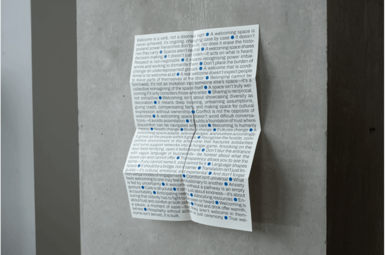 Photo of a leaflet. It is unfolded but the crease-marks are visible. It is entirely covered with grey text punctuated by bright blue dots. There is a slit in the centre of the paper.