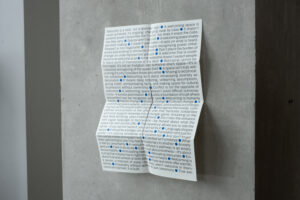 Photograph of a leaflet covered in printed text, punctuated by small bright blue dots.